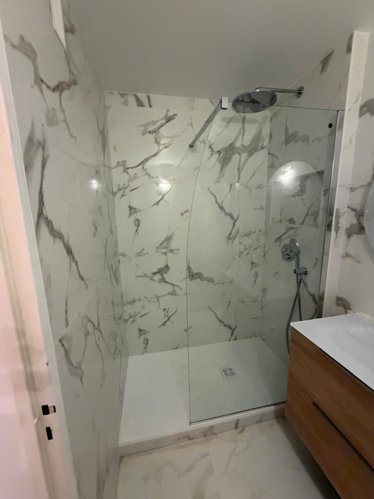 Salle de bain après rénovation avec douche vitrée et carrelage effet marbre