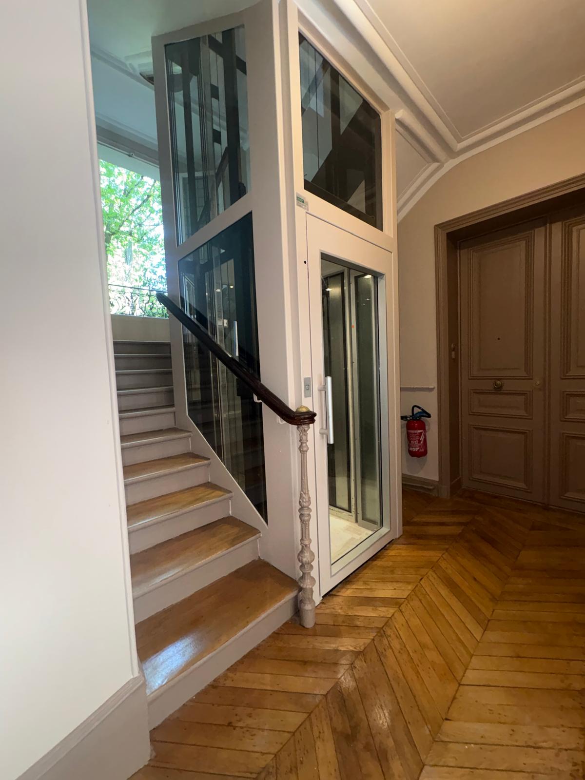 Cage d'escalier de copropriété rénovée avec parquet en point de Hongrie et ascenseur vitré